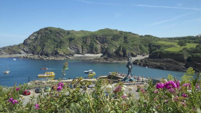 View seaside holiday cottages and apartments in Ilfracombe. Panoramic view of the entrance to Ilfracombe Harbour, guarded by a giant statue of a woman waving a sword.