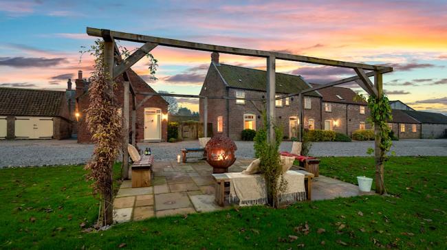 An arbour with a firepit in front of a row of stone barn conversions at sunset.