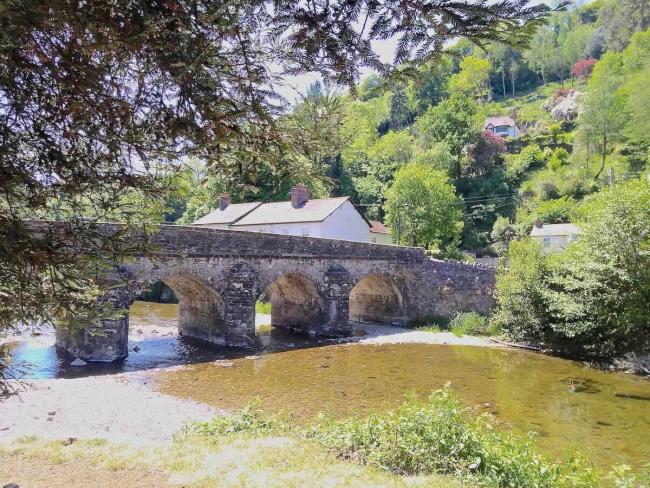 View Holiday Cottages in Dulverton in the Heart of Exmoor. A wide, shallow river flows under an old 4-arch stone bridge.