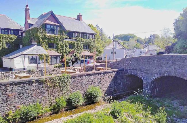 Find Holiday Cottages in Exford Available to Rent Exterior of a riverside pub next to a stone bridge.