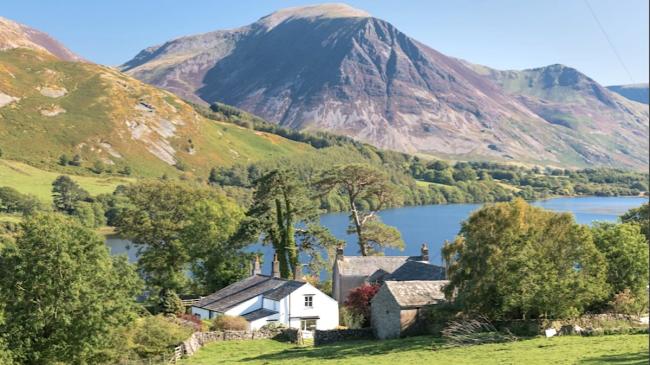 Lakeside Holiday Cottages in Cumbria A holiday cottage overlooks a large lake in front of tall Lake District Fells.