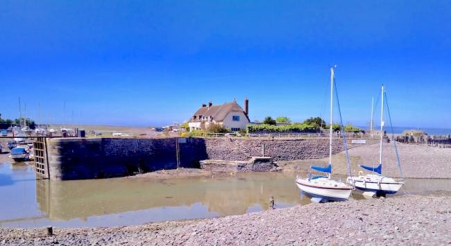 Porlock Weir- Stay in Somerset's Most Secret Seaside Village. Two yachts, overlooked by thatched cottages await an incoming tide to access a small harbour.