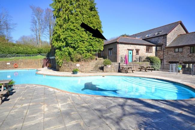 A small cottage attached to larger cottages overlooks a kidney-shaped outdoor pool in a garden.