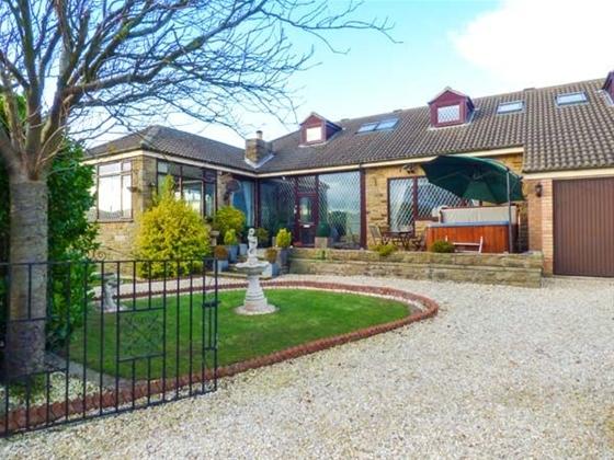 A large chalet bungalow with large glass windows and a hot tub on the front terrace.