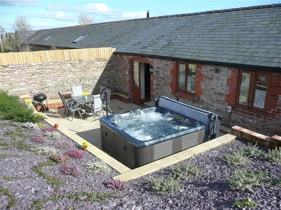Single storey exterior of a barn conversion with a hot tub on its terrace.