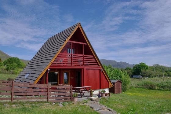 Exterior of a 2-storey, wooden A-Frame eco lodge surrounded by oprn countryside