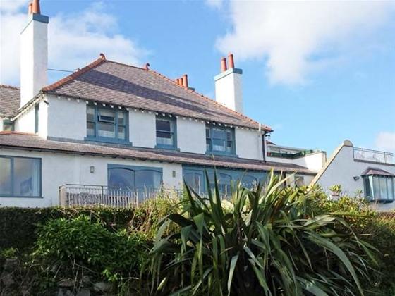 Exterior of a large holiday Anglesey holiday cottage with many windows  and terrace overlooking a shrub-filled garden.