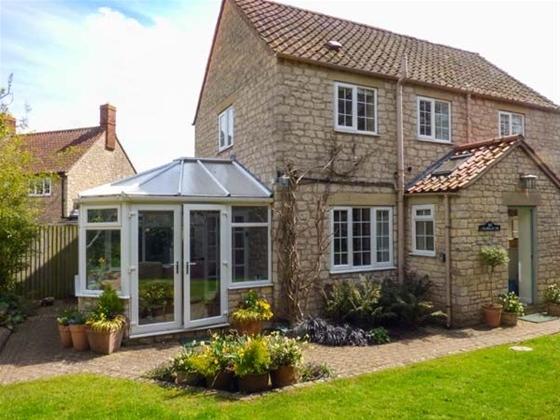 Exterior of a stone cottage with enclosed porch and sun lounge overlooking a lawn.
