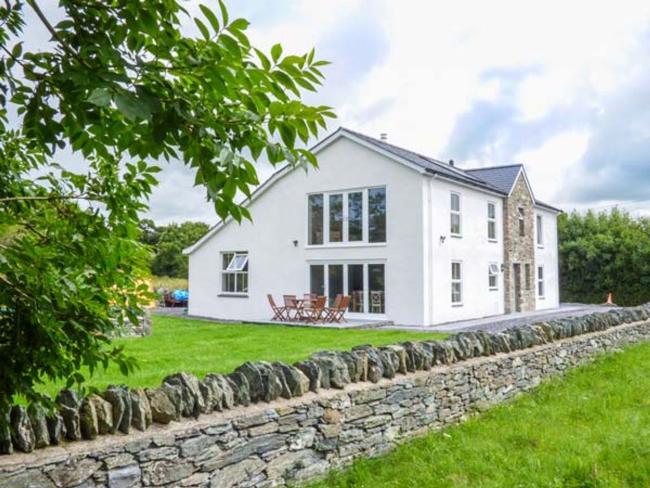 A large house with floor-to-ceiling windows surrounded by a large garden in the countryside.