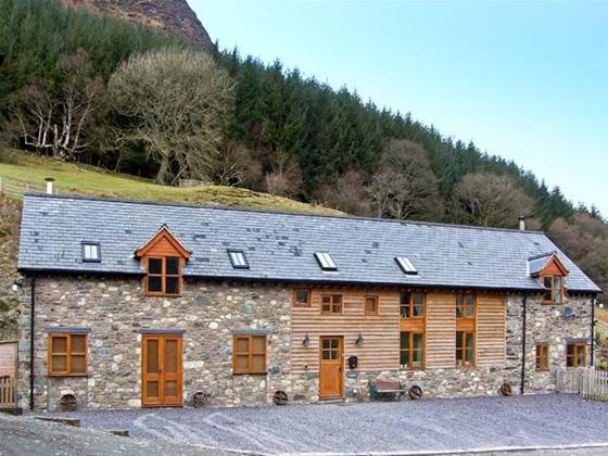 A slate-roofed, stone holiday cottage in Powys nestles beneath a step hill toppped with a wood.
