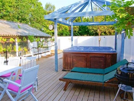 A hot tub beneath a glass roof sits on a wooden deck next to two sun loungers.
