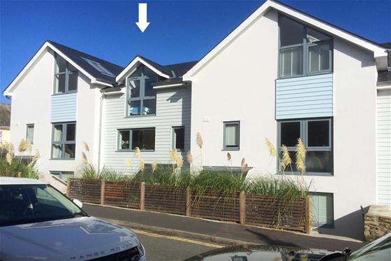 Exterior of a contemporary terraced seaside holiday cottage with floor-to-ceiling bedroom window.
