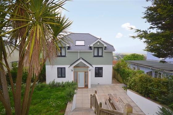 A modern, 2-storey, half-timbered house overlooks a long garden and paved terrace lined by palm trees.