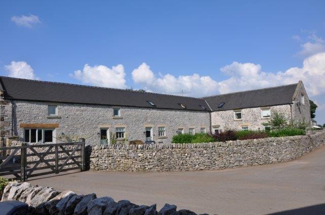 Converted barns overlook a courtyard garden bordered by a low stone wall.
