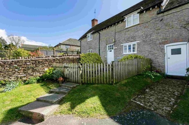 Exterior of a stone-built terraced cottage with a picket fence around the front garden.