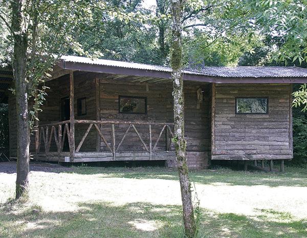 An eco-friendly log cabin with a fenced-in verandah sits in the shade of mature trees.