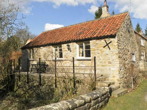A single storey stone built cottage with a raised terrace overlooking a garden.