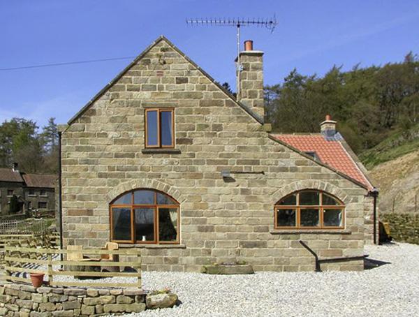 A stone-built North Yorkshire holiday cottage surrounded by woods and fields.