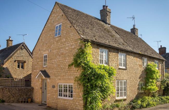 A semi-detached Cotswold honeystone cottage with wisteria-clad walls