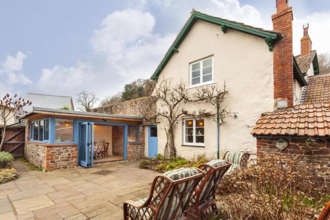 Exterior of a Dunster holiday cottage with a pave courtyard and sun loungers.