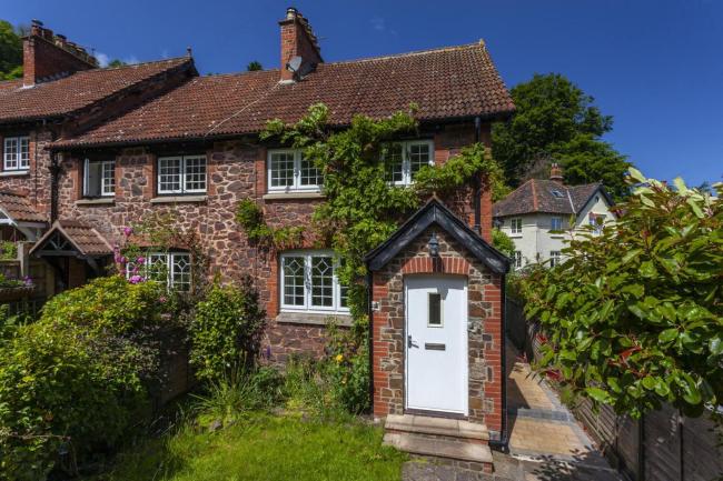 Exterior of a wisteria-clad stone-built holiday cottage in Porlock on a sunny day.