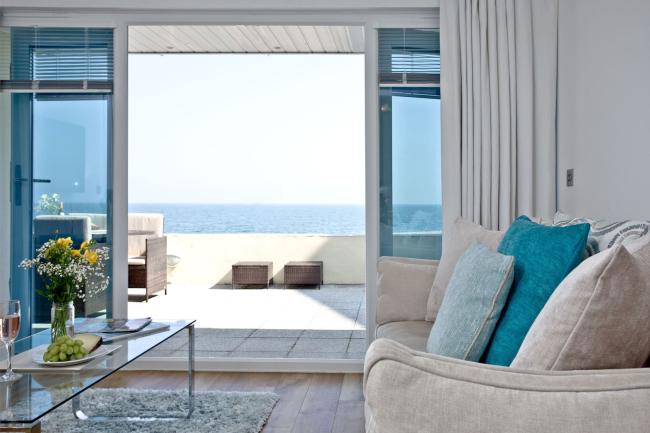 A lounge with comfortable sofas and TV has French windows with a sea view