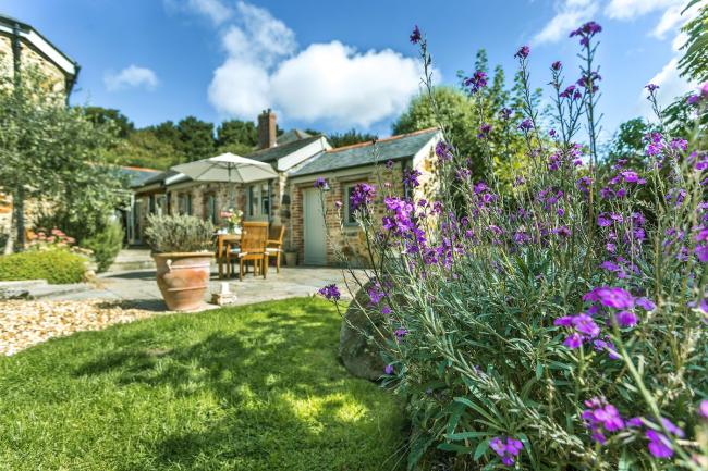 exterior view of a stone-built barn conversion amidst a garden full of mature shrubs, bushes and a lawn.
