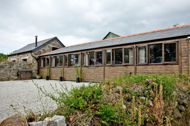A long single-storey barn conversion with a line of windows along one side overlooks a shingled driveway and garden.