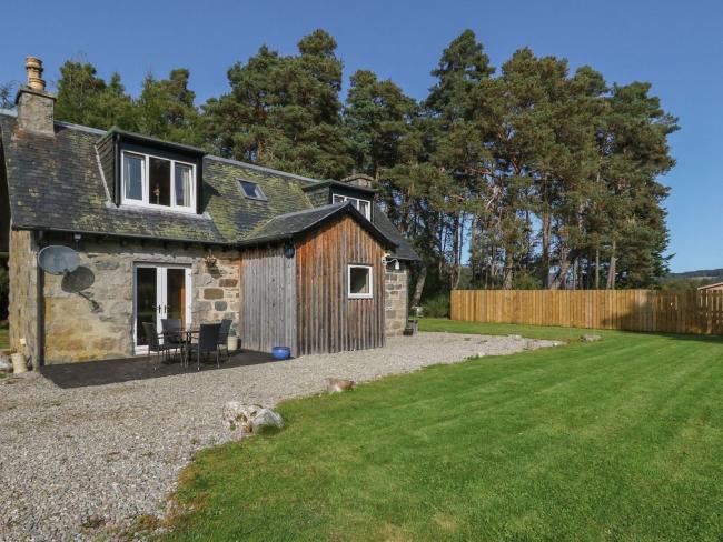 Backed by tall pine trees a 2-storey tone-built Newtonmore holiday cottage overlooks a large lawn.