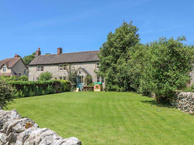Exterior of a stone-built house overlooking a lawn surrounded by a stone wall and small trees.
