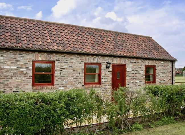 Exterior of a single-storey stone-built rural holiday cottage with a terrace and a front hedge.