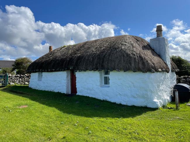 Exterior of a restored Scottish croft with stone walls thatched roof in a remote location on Skye