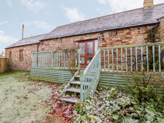 Single-storey brick-built barn conversion forming a holiday cottage with a long deck and lawned garden with a light sprinkling of winter snow. overlooking a