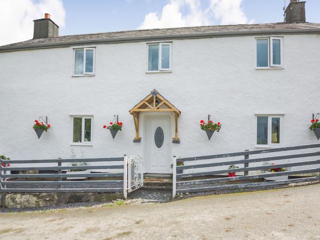 Front exterior of a double-fronted2-storey  Welsh holiday cottage with wall-mounted flowerpots and a wooden fence.