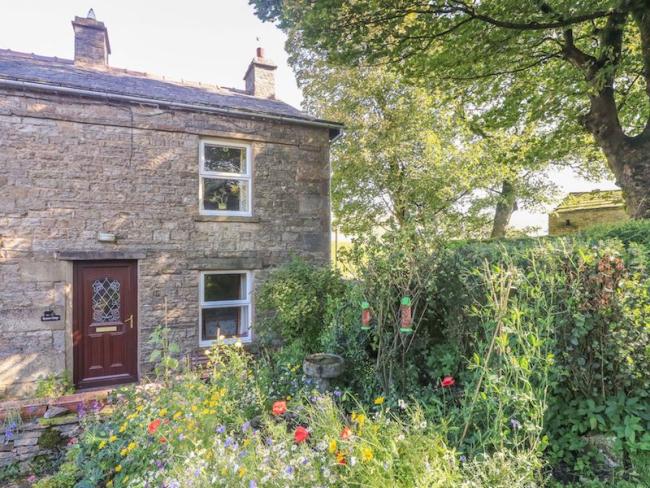 A stone built country cottage in the Yorkshire Dales overlooks a mature garden with flowering poppie.