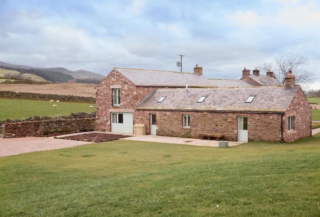 Exterior of a Cumbriain stone. barn conversion near surrounded by fields.