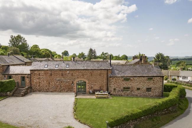 Exteriorof a large stone-built hall in Cumbria with a large lawn and parking spaces.