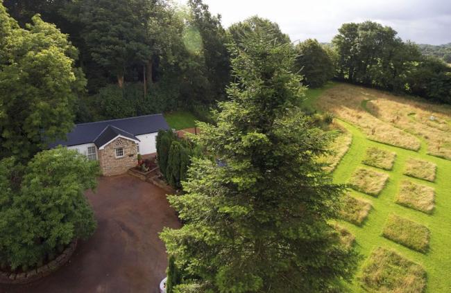 Aerial view of a country cottage on the edge of a wood overlooking fields in Glamorgan