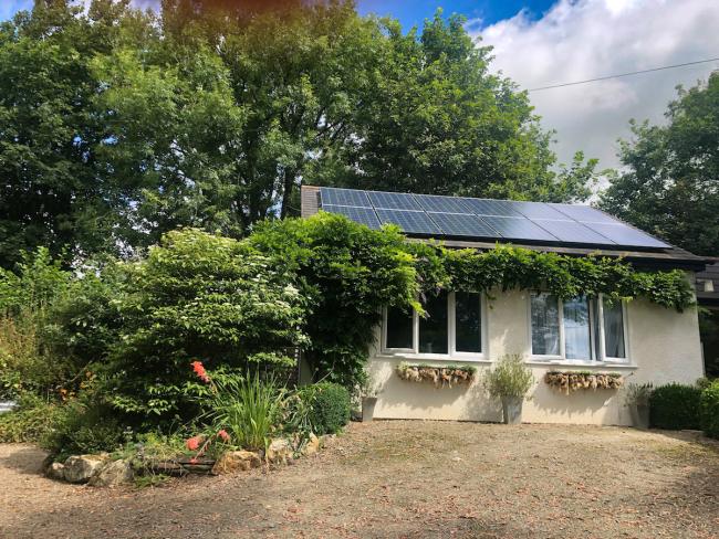 Exterior of a single-storey, vine-dlad, one bedroom holiday bungalow near Bude overlooked by mature trees.