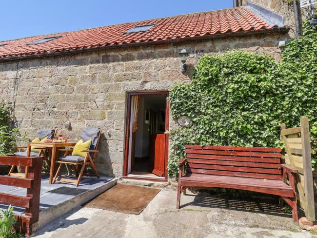 A cosy stone-built cottage in Danby on a sunny day with a garden bench and patio.
