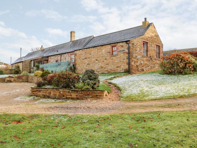 A single-storey, stone-built barn conversion in Cumbria with parking spaces and lawns.