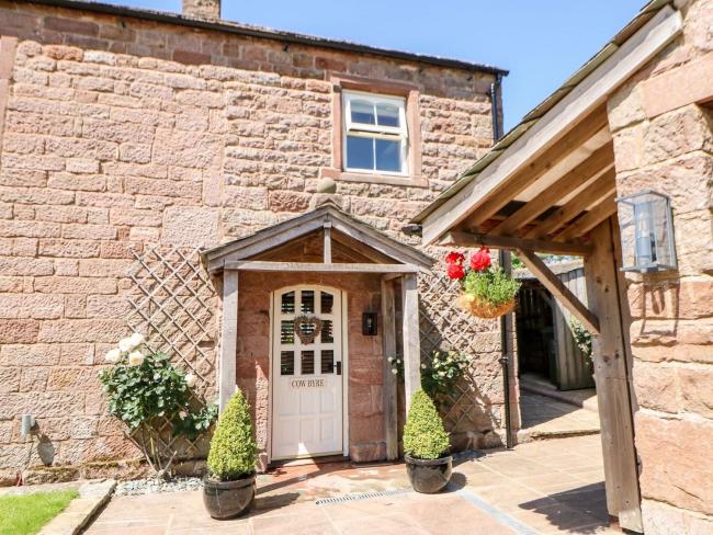 Entrance to a stone-built Cumbrian coottage with a porch and small lawn.