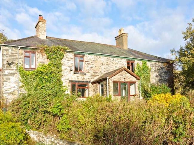 Frontage of a creeper-clad stone farmhouse overlooking mature gardens.