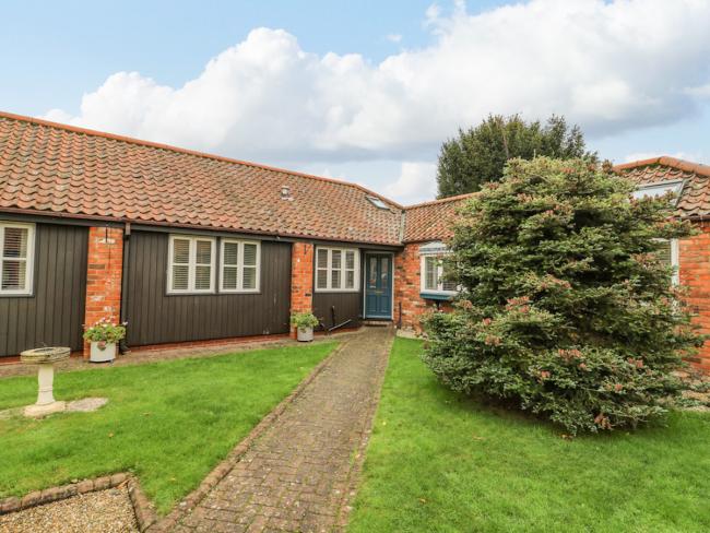 A single-storey wooden brick path crosses a lawn to the front door of wooden barn conversion 