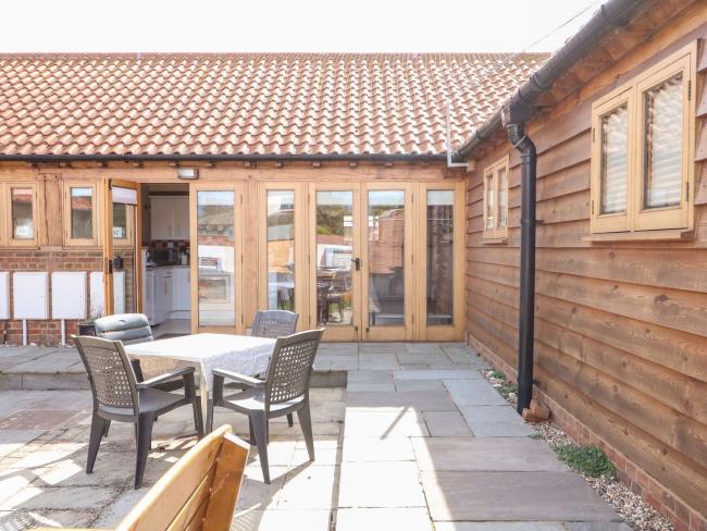 L-shaped exterior of a wooden barn conversion with floor-to-ceiling folding windows.