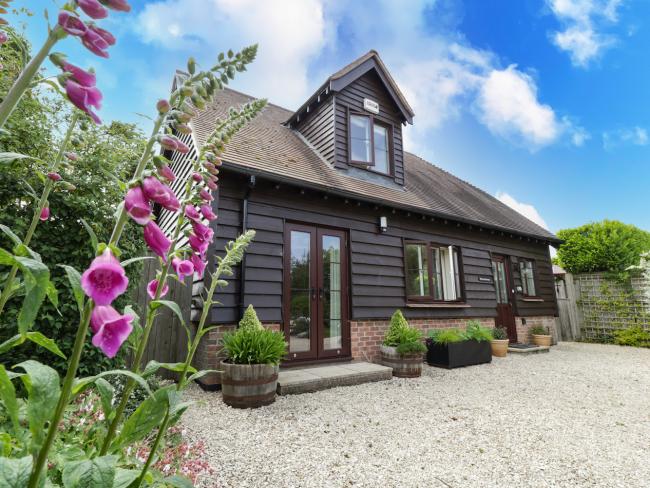 Exterior of a 2-storey wooden cottage overlooking a large drive bordered by flowers.