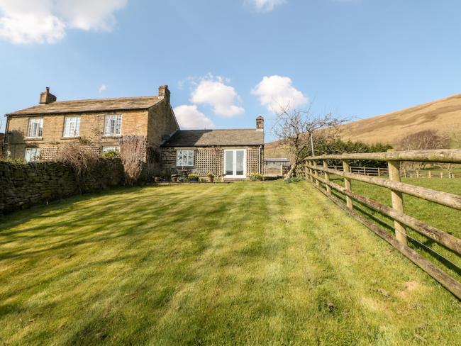 A large cottage with a ground floor extension is surrounded by open fields and moorland.