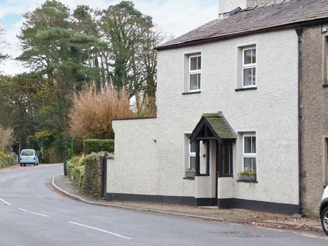 A white-rendered cottage with a small porch overlooks a village street.