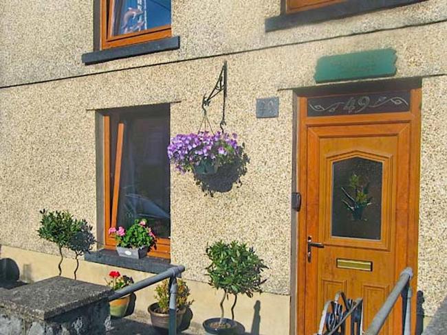 A pebble-dash, terraced holiday cottage in Ammanford with table and chairs for two in the front garden.