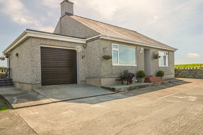 A countryside holiday bungalow in Anglesey with a garage and surrounded by fields.